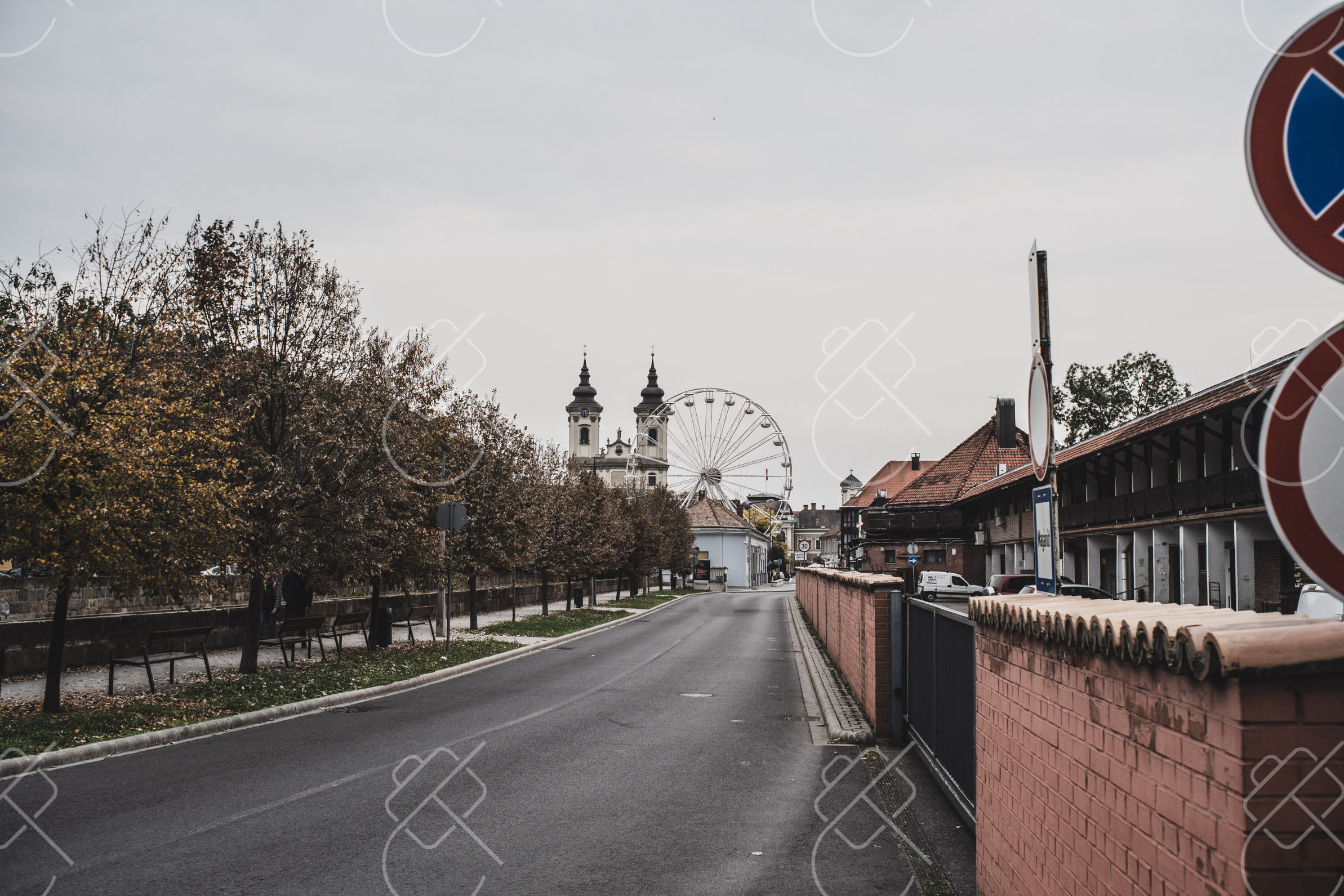 The basilica's twin towers and the town's fairground wheel at the end of a tree-lined street — Eger, fine art travel photography print available from Clever Tourists