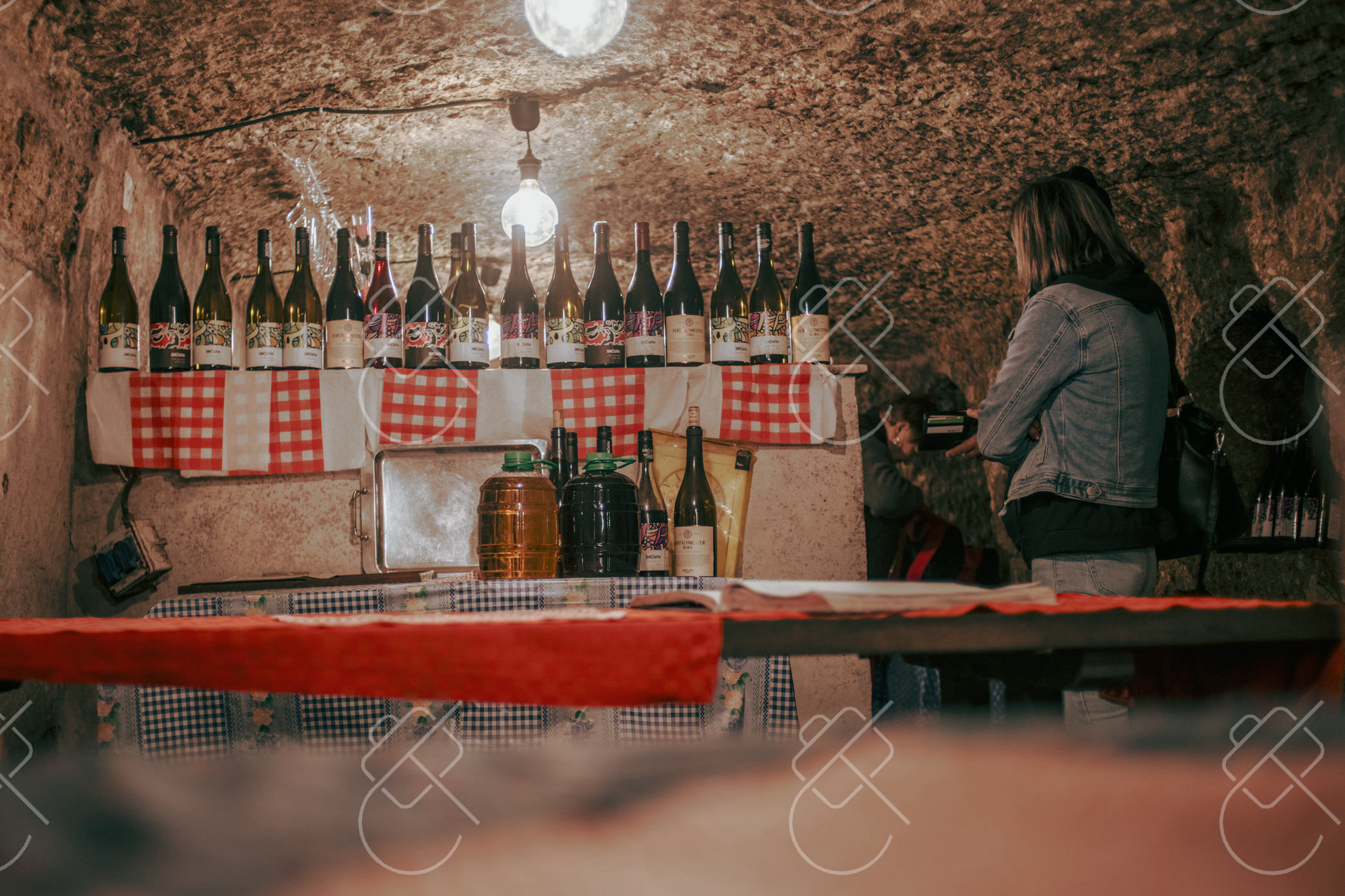 A cellar cut into the rock in Szépasszony-völgy, bottles lined up under checked cloths — Eger, fine art travel photography print available from Clever Tourists