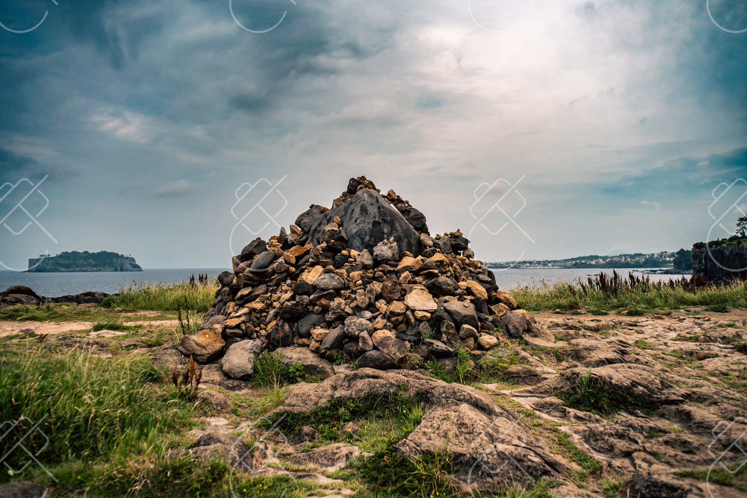 A stacked stone cairn on the coastal trail outside Seogwipo, with an offshore island beyond — Seogwipo, fine art travel photography print available from Clever Tourists