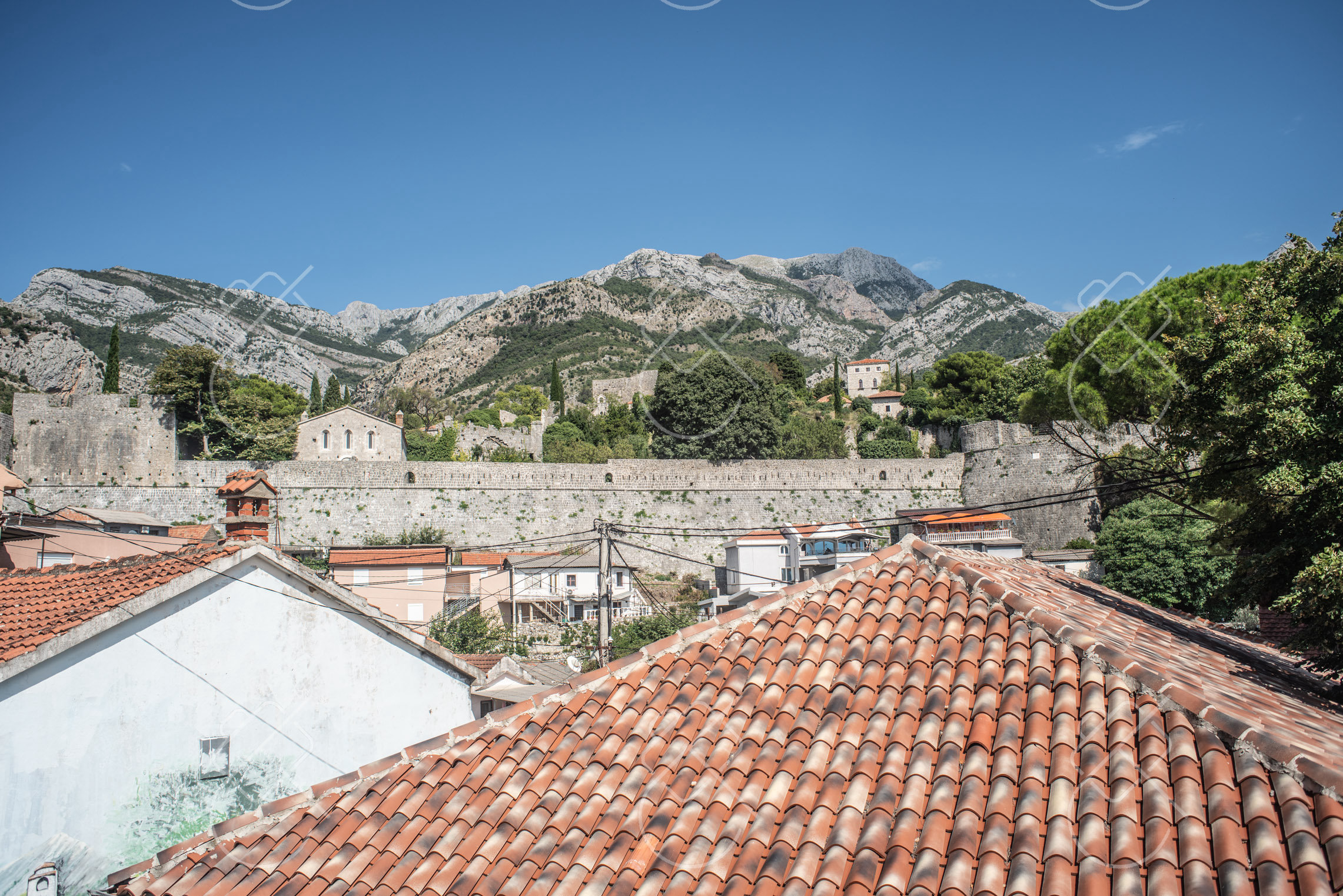 Terracotta rooftops and ruin walls beneath the mountains behind Stari Bar — Stari Bar, fine art travel photography print available from Clever Tourists
